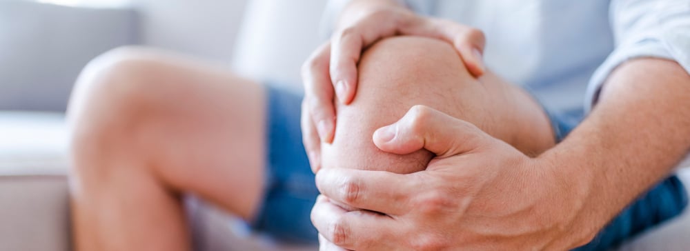 A man sitting on the couch in pain holding his injured knee