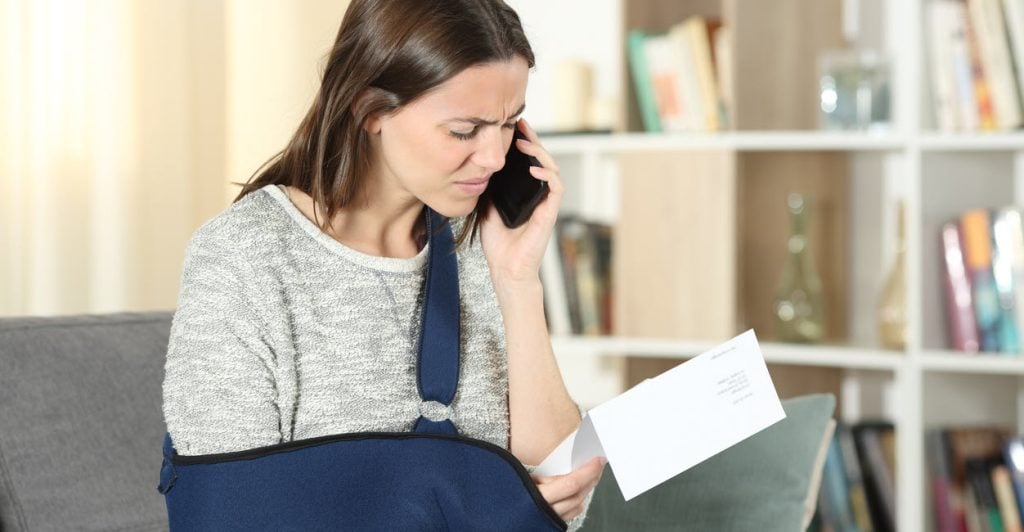 Upset woman with injured arm reviews her settlement documents on the phone