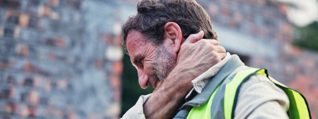 Trabajador con una lesión en el cuello, agarrándose el cuello y haciendo muecas de dolor